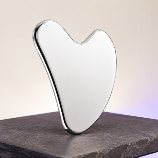 Polished stainless steel gua sha tool on a charcoal stone surface